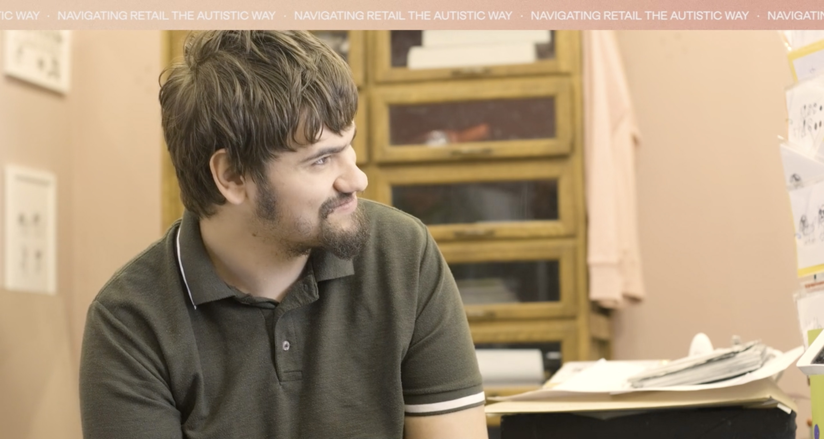 A boy with a beard sits side profile, he is happy and smiling.